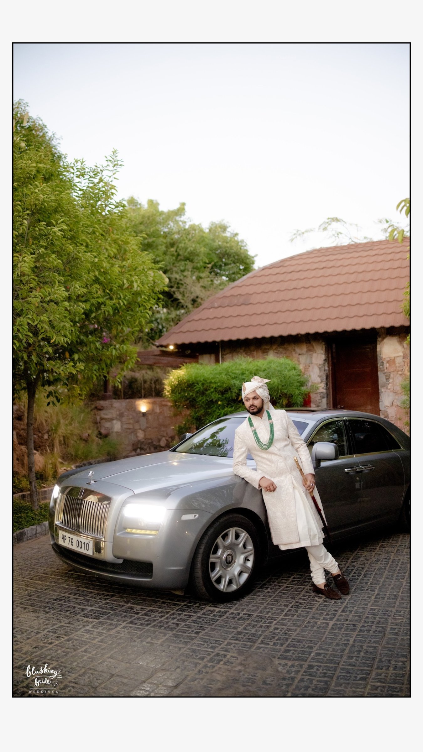 Groom standing beside a silver luxury wedding car at a resort