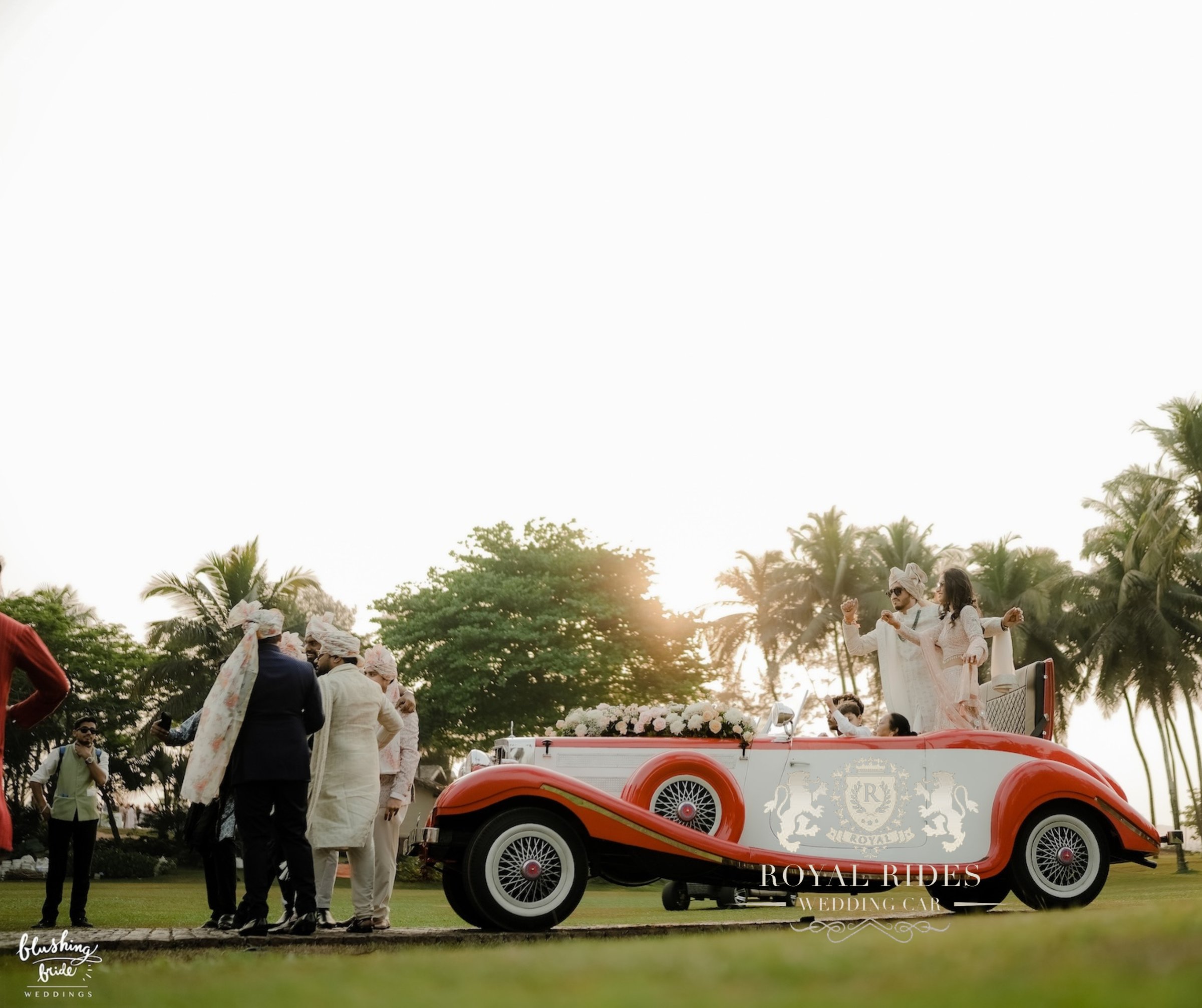 Groom's party walking beside the red and white vintage car at sunset