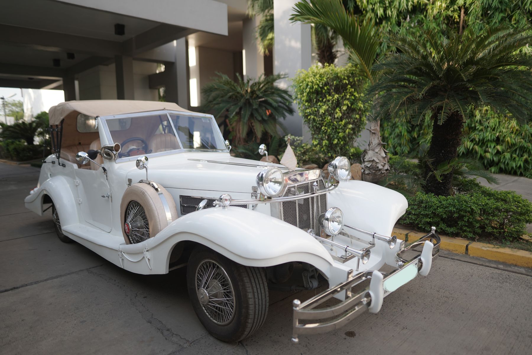 White vintage car with convertible hood parked at a hotel porch